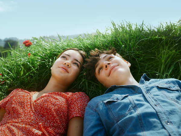 Mädchen und Junge liegen auf einer Wiese und blicken verträumt in den Himmel.
